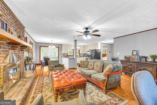 living room with a textured ceiling, light hardwood / wood-style floors, crown molding, ceiling fan with notable chandelier, and a brick fireplace