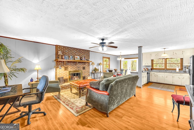 living room featuring sink, light wood-type flooring, a brick fireplace, and a textured ceiling