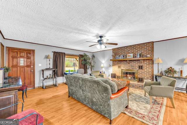 living room featuring a brick fireplace, light hardwood / wood-style flooring, a textured ceiling, crown molding, and ceiling fan