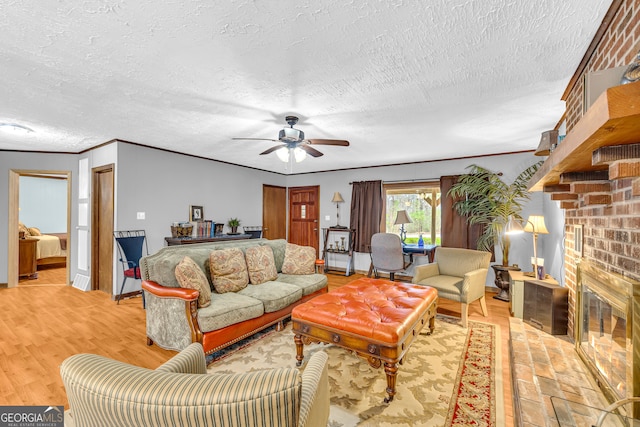 living room with a brick fireplace, light hardwood / wood-style floors, ceiling fan, a textured ceiling, and crown molding