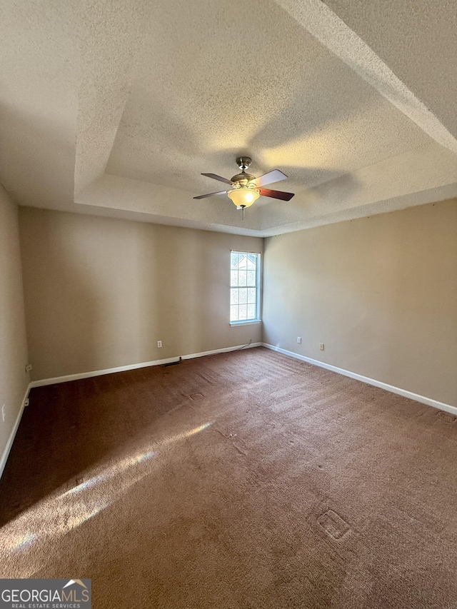 unfurnished room featuring a raised ceiling, carpet, ceiling fan, and a textured ceiling