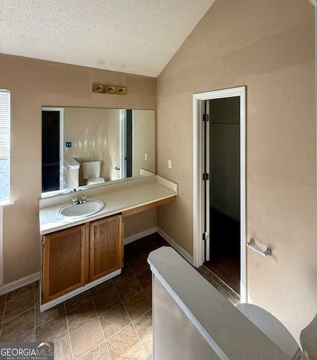 bathroom with toilet, a textured ceiling, vaulted ceiling, tile patterned floors, and vanity