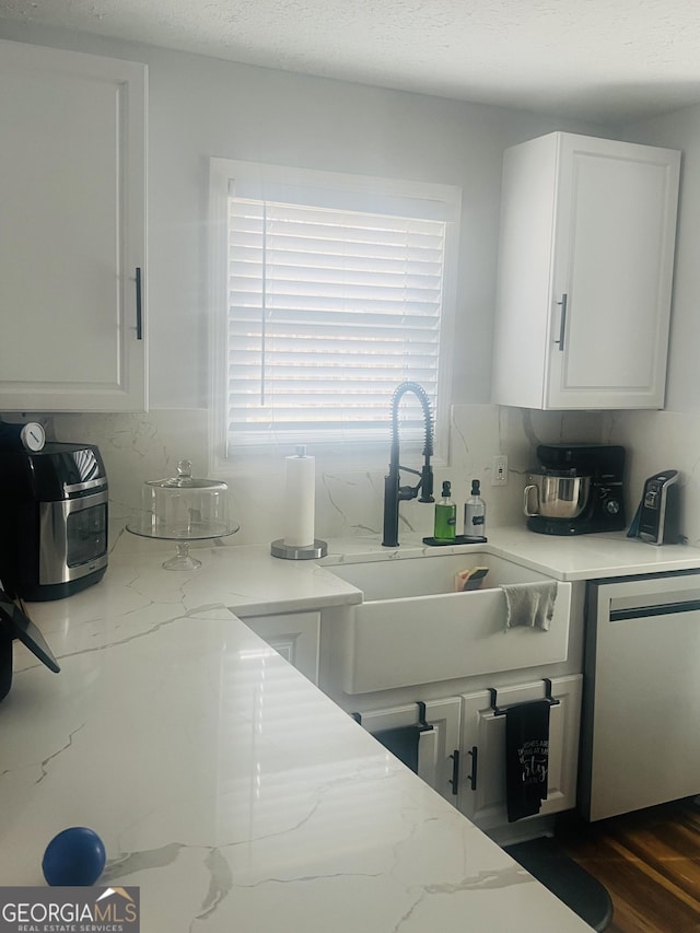 kitchen featuring sink, dishwasher, white cabinetry, and light stone countertops