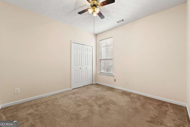 unfurnished bedroom featuring a textured ceiling, a closet, light colored carpet, and ceiling fan