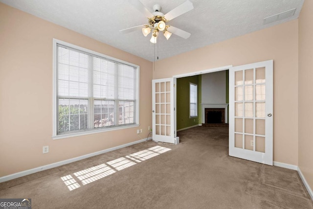 unfurnished room featuring a fireplace, french doors, carpet floors, ceiling fan, and a textured ceiling