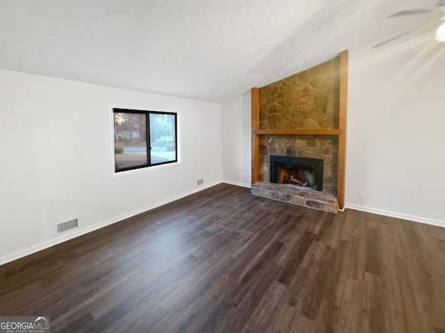 unfurnished living room with dark wood-style flooring, lofted ceiling, visible vents, a stone fireplace, and baseboards