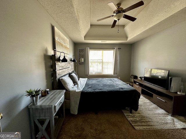 bedroom featuring a textured ceiling, dark carpet, ceiling fan, and a raised ceiling
