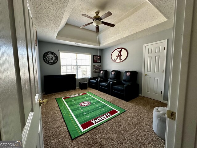 rec room featuring a tray ceiling, ceiling fan, carpet, and a textured ceiling