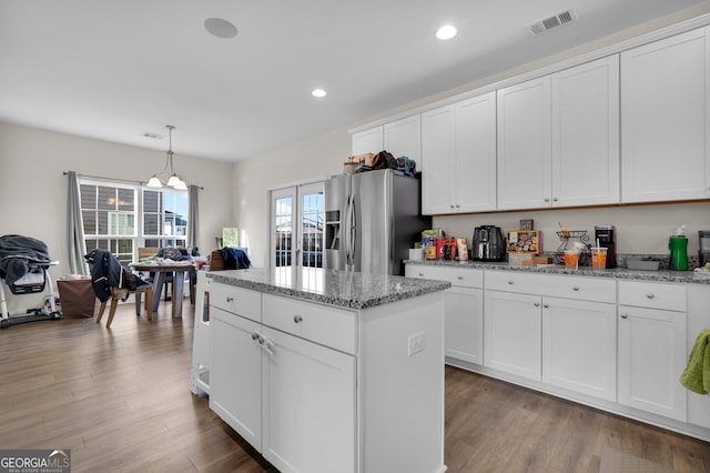 kitchen featuring stainless steel fridge with ice dispenser, hanging light fixtures, a center island, light stone counters, and white cabinets