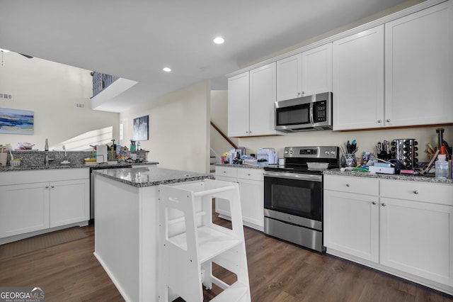 kitchen with appliances with stainless steel finishes, stone countertops, dark wood-type flooring, a center island, and white cabinetry