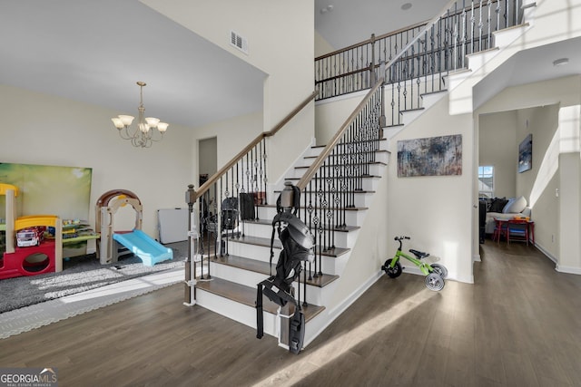 stairs featuring an inviting chandelier, hardwood / wood-style flooring, and a high ceiling