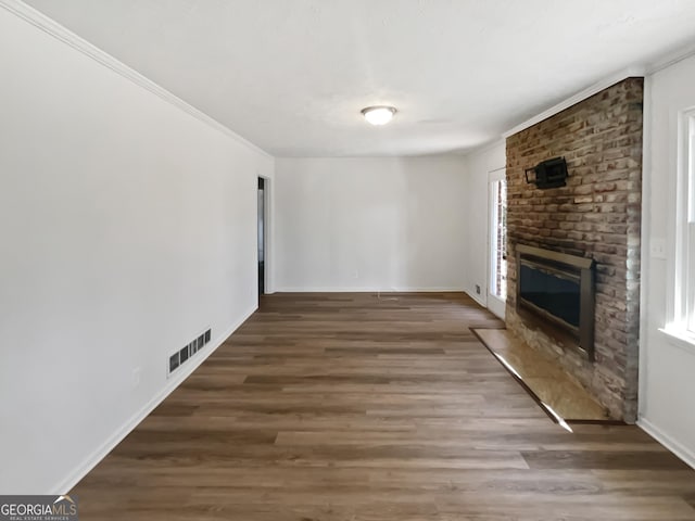 unfurnished living room featuring dark wood-type flooring, a brick fireplace, visible vents, and crown molding