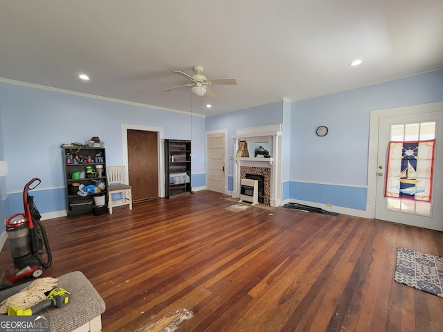 unfurnished living room featuring a fireplace, dark wood-type flooring, crown molding, and ceiling fan