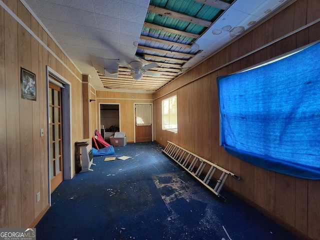 miscellaneous room featuring ceiling fan, dark colored carpet, and wooden walls