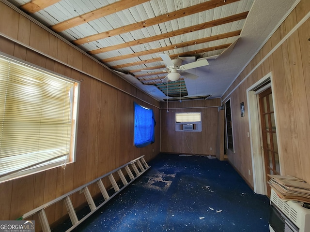 unfurnished room featuring a healthy amount of sunlight, dark colored carpet, and wood walls