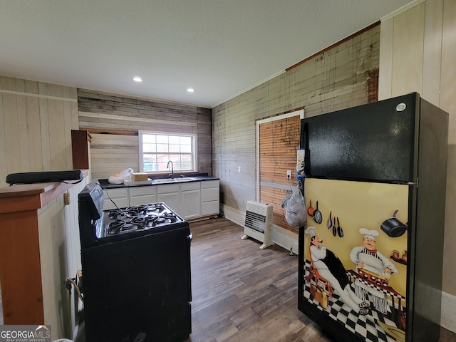 kitchen with black appliances, wood walls, dark hardwood / wood-style flooring, sink, and white cabinetry