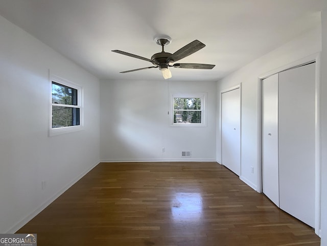 unfurnished bedroom with ceiling fan, dark hardwood / wood-style flooring, and two closets