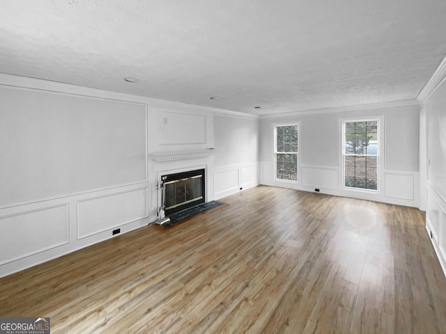 unfurnished living room with light wood finished floors, a fireplace with flush hearth, a decorative wall, and crown molding