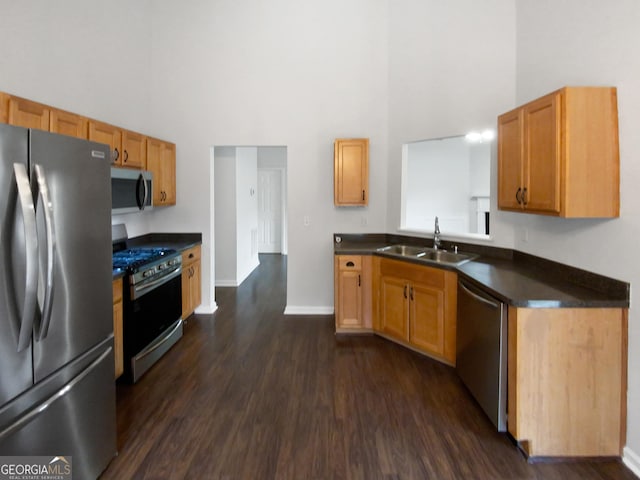 kitchen with stainless steel appliances, a high ceiling, dark countertops, and a sink