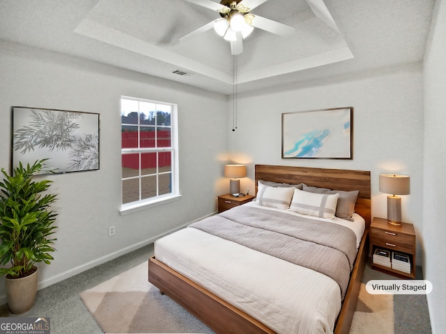 bedroom with light carpet, visible vents, baseboards, ceiling fan, and a tray ceiling