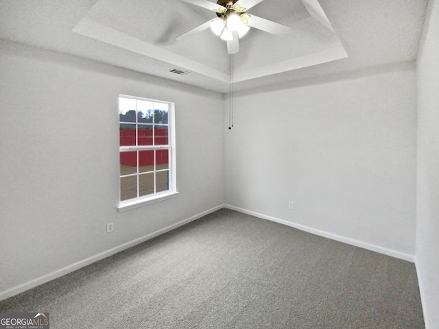 carpeted empty room with a ceiling fan, a raised ceiling, visible vents, and baseboards