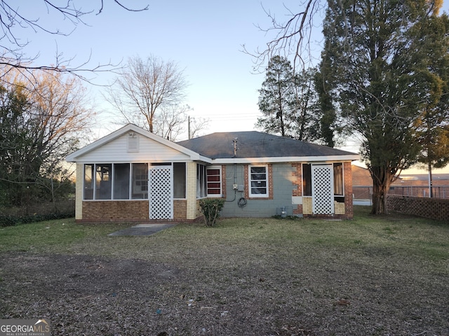 back house at dusk featuring a lawn and a sunroom