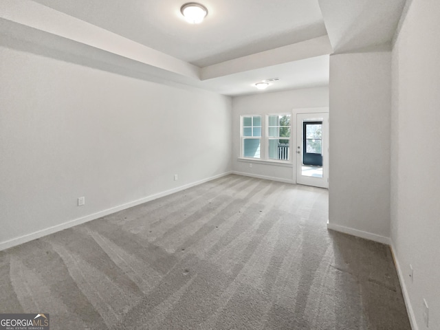 carpeted empty room featuring a raised ceiling and baseboards