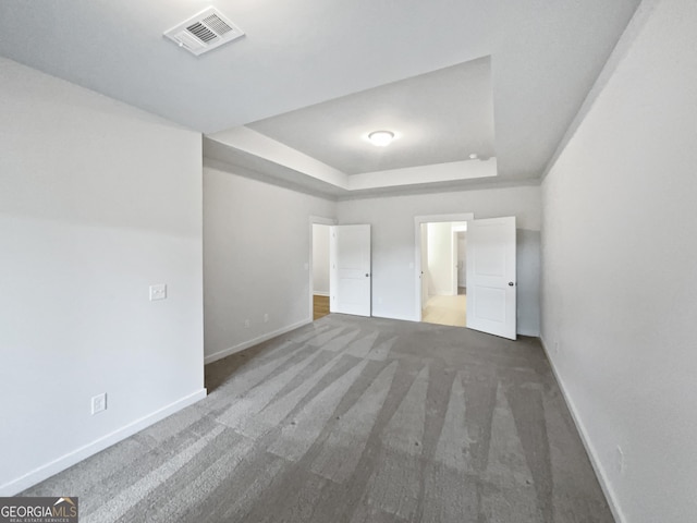 unfurnished bedroom featuring a tray ceiling, visible vents, dark carpet, and baseboards