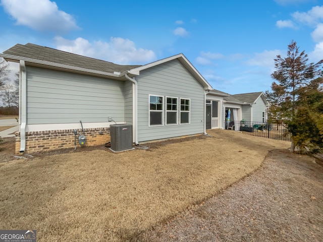 back of property with central air condition unit, fence, and a lawn