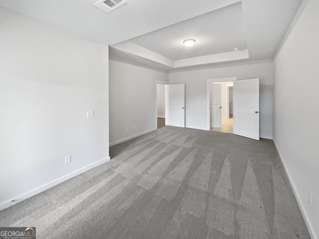 unfurnished bedroom with a tray ceiling, visible vents, baseboards, and dark colored carpet