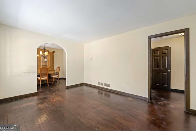 spare room featuring dark hardwood / wood-style flooring and an inviting chandelier