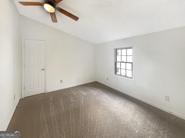 empty room with vaulted ceiling, dark carpet, and ceiling fan