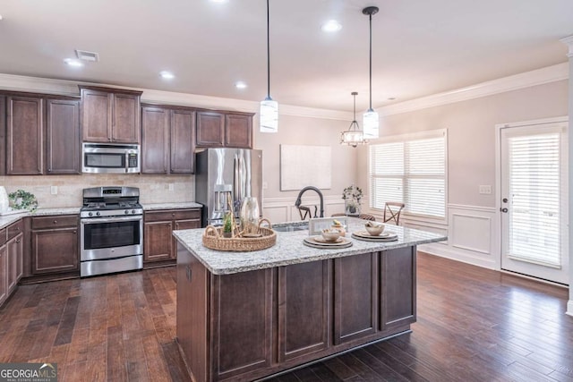 kitchen featuring a center island with sink, appliances with stainless steel finishes, light stone countertops, and hanging light fixtures