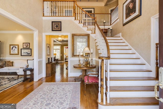 stairs with ornamental molding, baseboards, a high ceiling, and wood finished floors