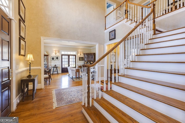 foyer featuring baseboards, stairway, ornamental molding, wood finished floors, and a high ceiling