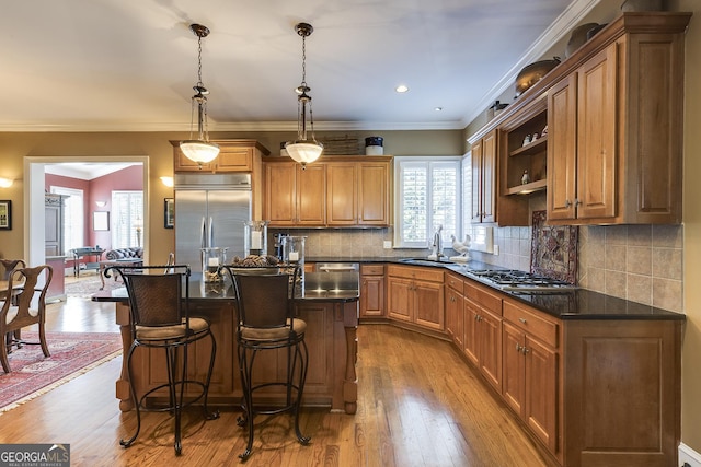 kitchen featuring brown cabinetry, an island with sink, dark countertops, appliances with stainless steel finishes, and pendant lighting