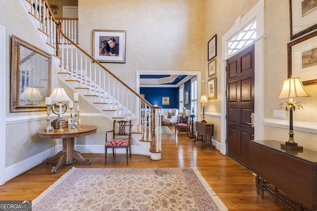 foyer entrance featuring stairway, a towering ceiling, baseboards, and wood finished floors