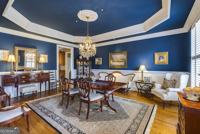 dining space with a chandelier, a wainscoted wall, a raised ceiling, and light wood-style floors