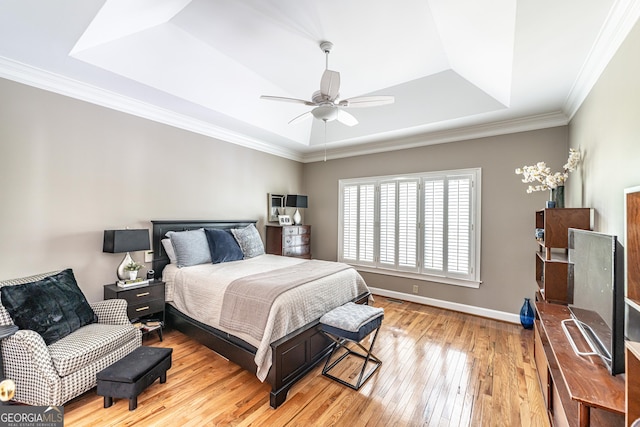 bedroom with crown molding, ceiling fan, baseboards, a tray ceiling, and hardwood / wood-style flooring