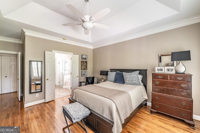 bedroom featuring crown molding, baseboards, light wood-style flooring, and a tray ceiling