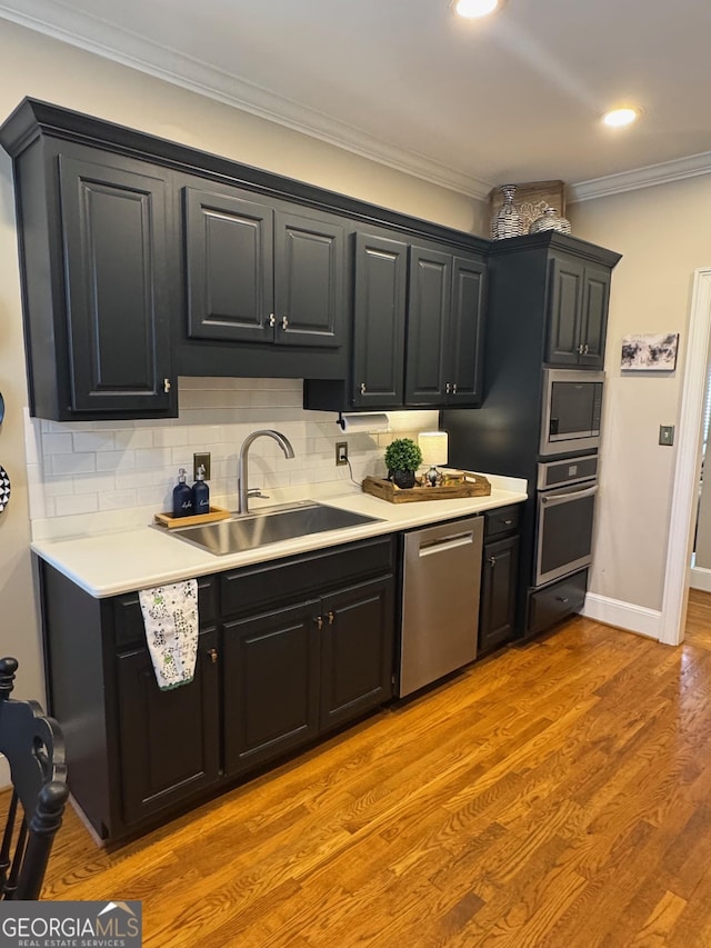 kitchen with crown molding, stainless steel appliances, light countertops, a sink, and light wood-type flooring