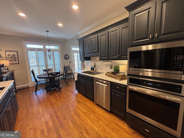 kitchen with a sink, light wood-style floors, light countertops, ornamental molding, and appliances with stainless steel finishes