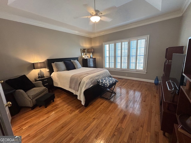 bedroom with baseboards, a ceiling fan, hardwood / wood-style floors, a tray ceiling, and crown molding