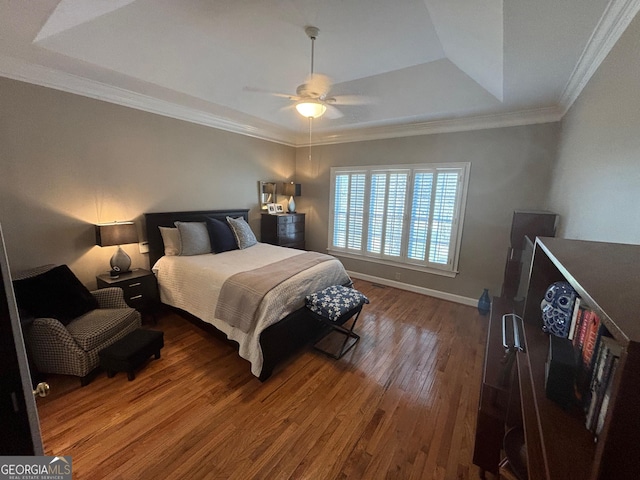 bedroom featuring a tray ceiling, crown molding, wood-type flooring, a ceiling fan, and baseboards