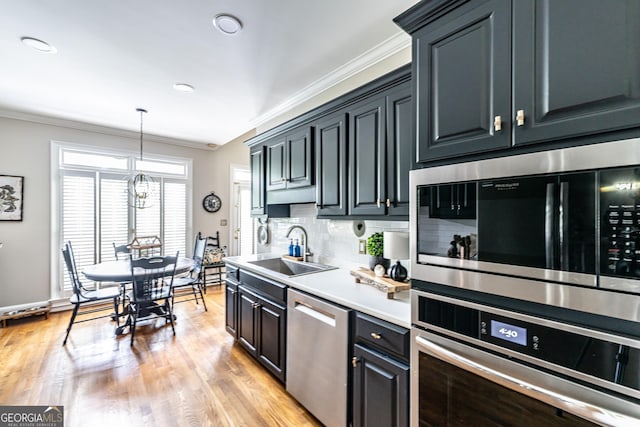 kitchen with decorative backsplash, a sink, light countertops, ornamental molding, and stainless steel appliances