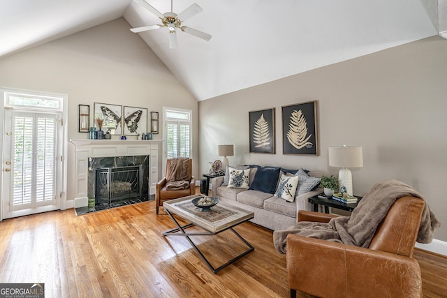 living area featuring ceiling fan, a fireplace, high vaulted ceiling, light wood-style flooring, and baseboards