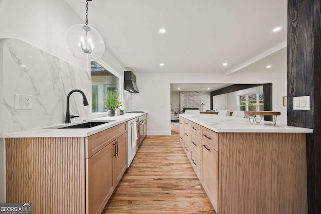 kitchen with sink, light wood-type flooring, decorative light fixtures, wall chimney range hood, and light brown cabinetry