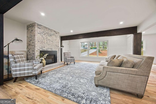 living room with a brick fireplace, light hardwood / wood-style flooring, and beamed ceiling