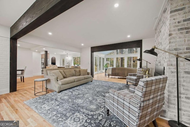 living room featuring light wood-type flooring, beamed ceiling, and brick wall