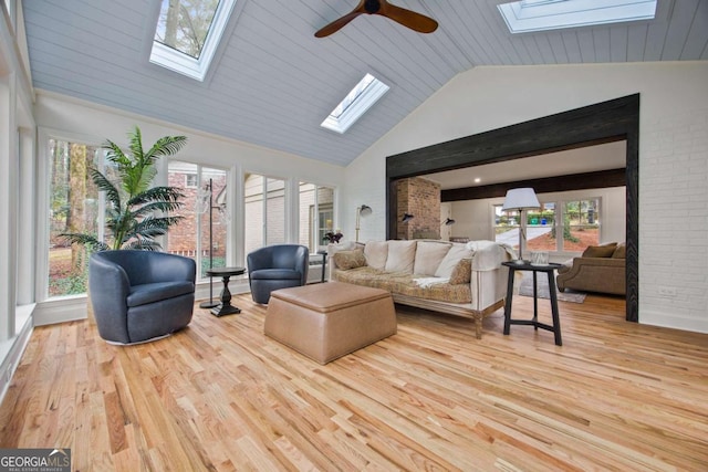 living room with a skylight, high vaulted ceiling, brick wall, and light hardwood / wood-style flooring